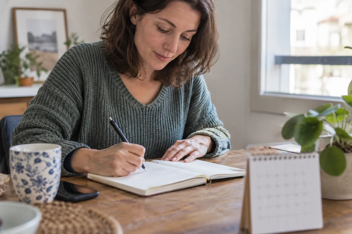 Une personne prépare des notes à une table, avec un carnet et un calendrier à proximité.