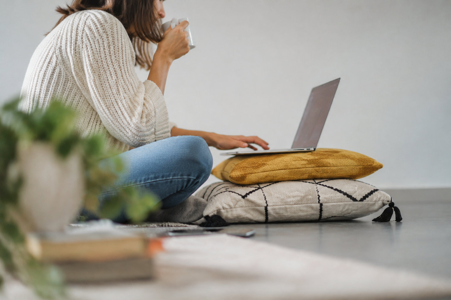 Une femme assise au sol utilisant son ordinateur portable avec une tasse à la main pour comparer sa mutuelle santé.